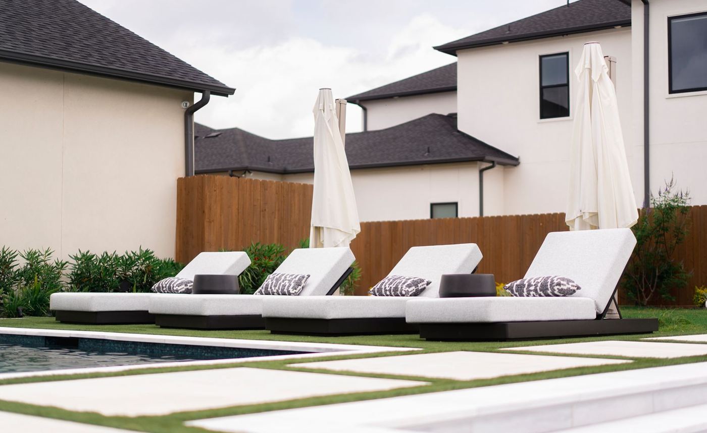 Row of white lounge chairs on a pool deck with large concrete pavers