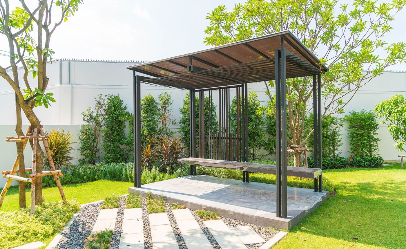 Dark-framed pergola with a wood roof over a stone platform in a garden