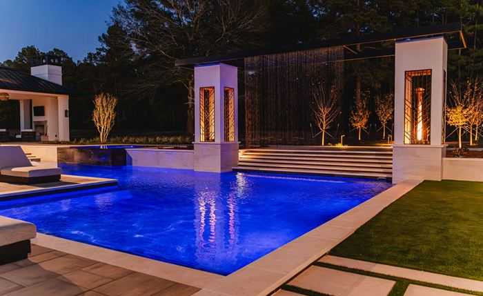 Modern pool with lit stone columns and a manicured lawn