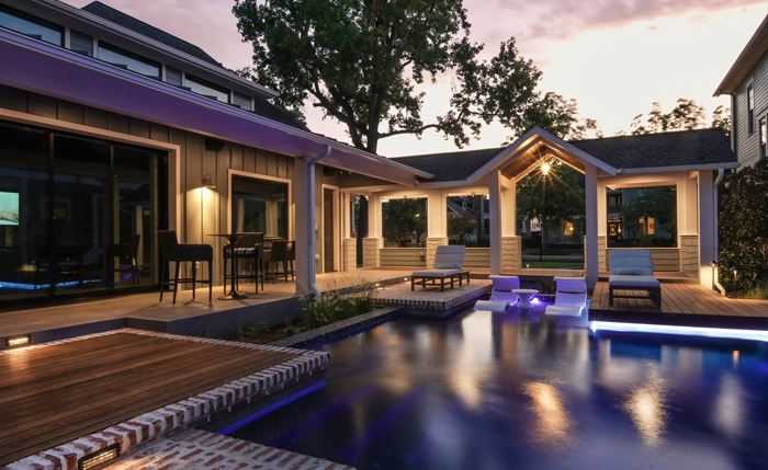 Luxury residential pool beside a covered patio and wood deck at dusk