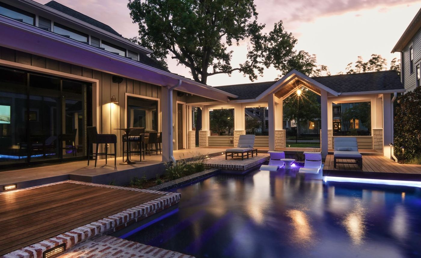 Luxury residential pool beside a covered patio and wood deck at dusk