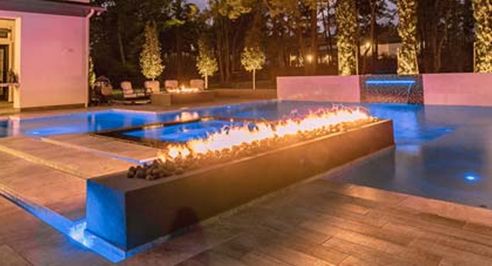 Fire bowls glowing beside a backyard pool at dusk