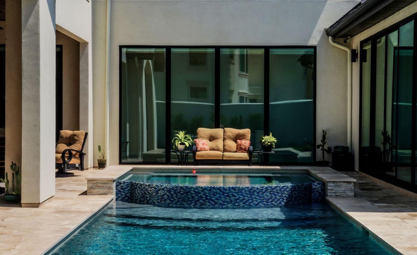Courtyard residential pool with a tiled raised spa and outdoor sofa beside glass doors