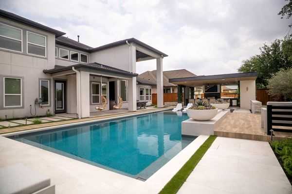 Modern backyard pool with a raised planter and covered patio beside a two-story home