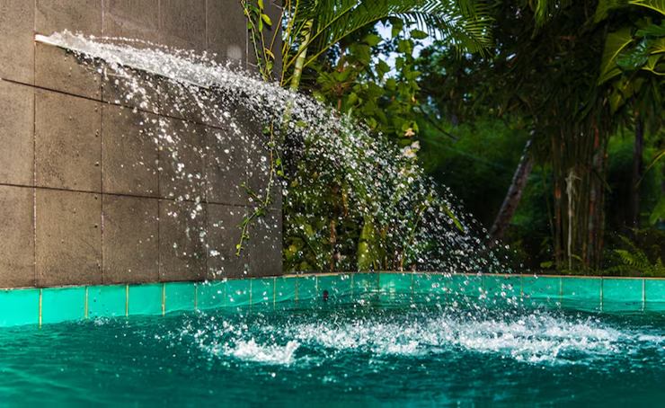 Backyard pool with a raised spa spilling water and a fire bowl